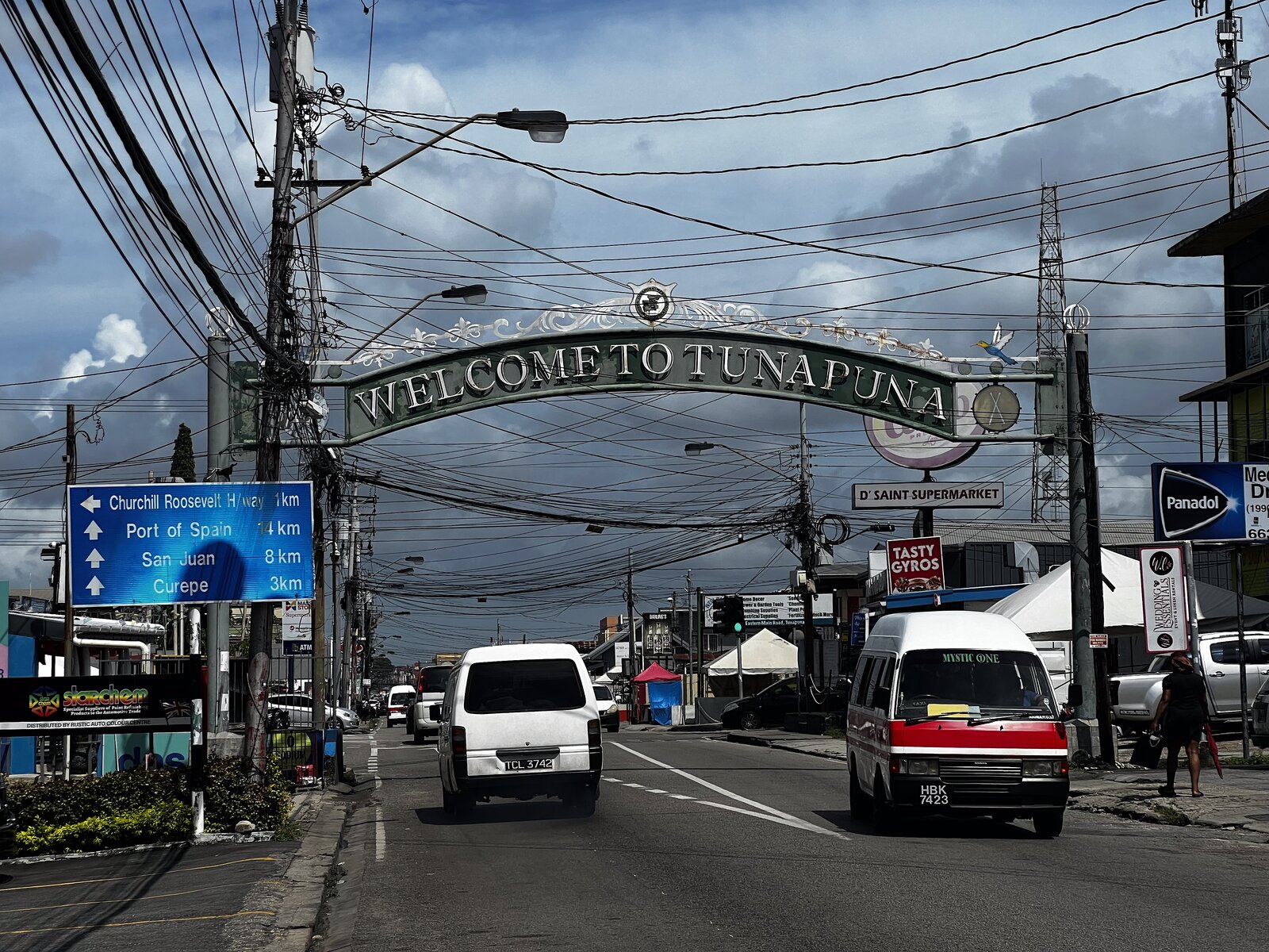 The 'Welcome to Tunapuna' arch over Eastern Main Road, with maxi taxis and traffic underneath.
